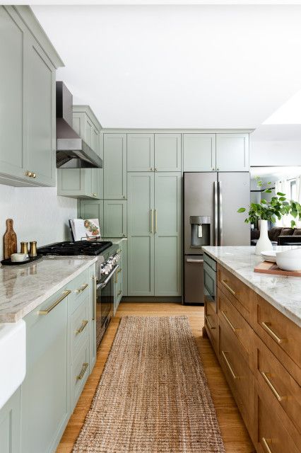 A modern sage green farmhouse kitchen with shaker cabinets, a stained island, neutral stone countertops, and gold fixtures