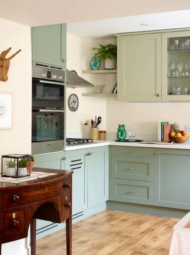 a modern sage green kitchen with shaker cabinets and glass fronts, a white backsplash and countertops, and a vintage sideboard