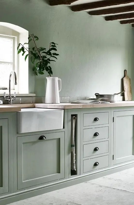 A sage green kitchen with a white ceiling and appliances and black handles looks ethereal and very natural