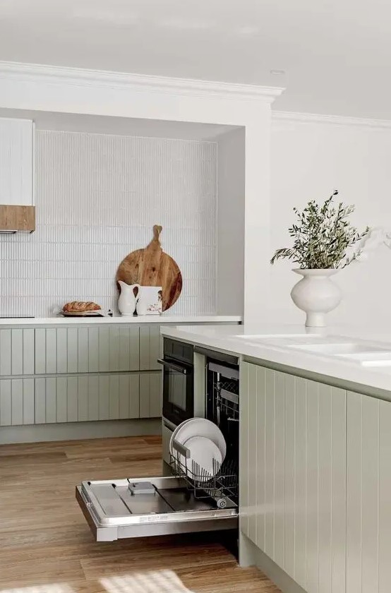 An airy modern kitchen with sage green slatted lower cabinets, a white thin tile backsplash and white stone countertops