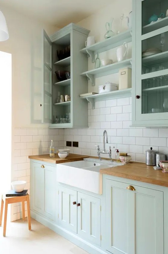 A chic mint green farmhouse kitchen with shaker-style cabinets, butcher block countertops, a white subway tile backsplash, and a vintage faucet
