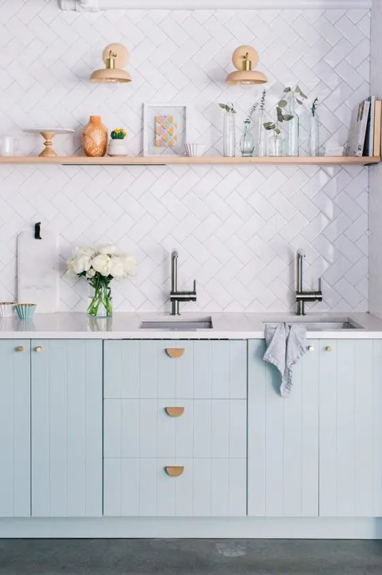 A beautiful kitchen with light blue kitchen cabinets, a white tile backsplash and white countertops, as well as an open shelf for displaying things