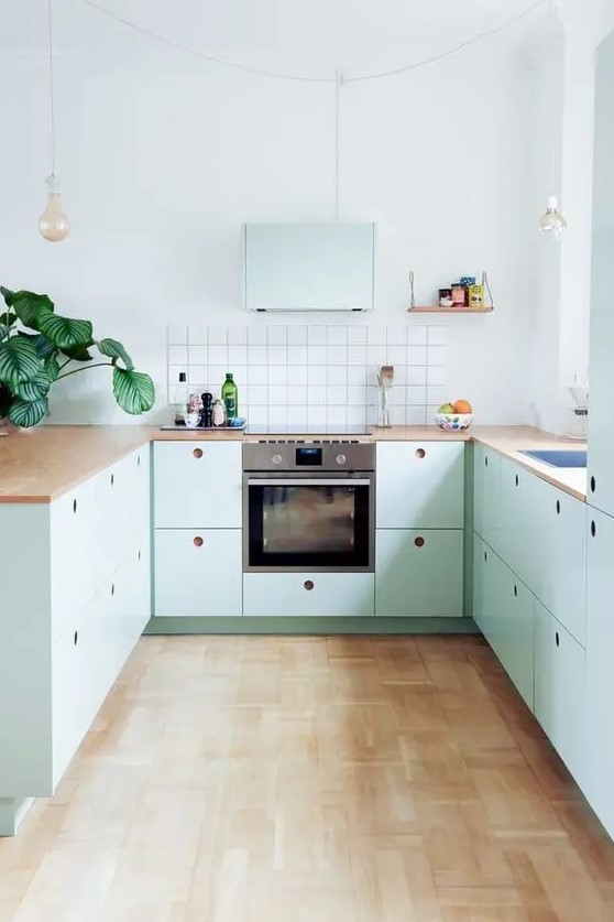 A beautiful mint blue Scandinavian kitchen with plywood cabinets, butcher block countertops, a square tile backsplash, and hanging lamps