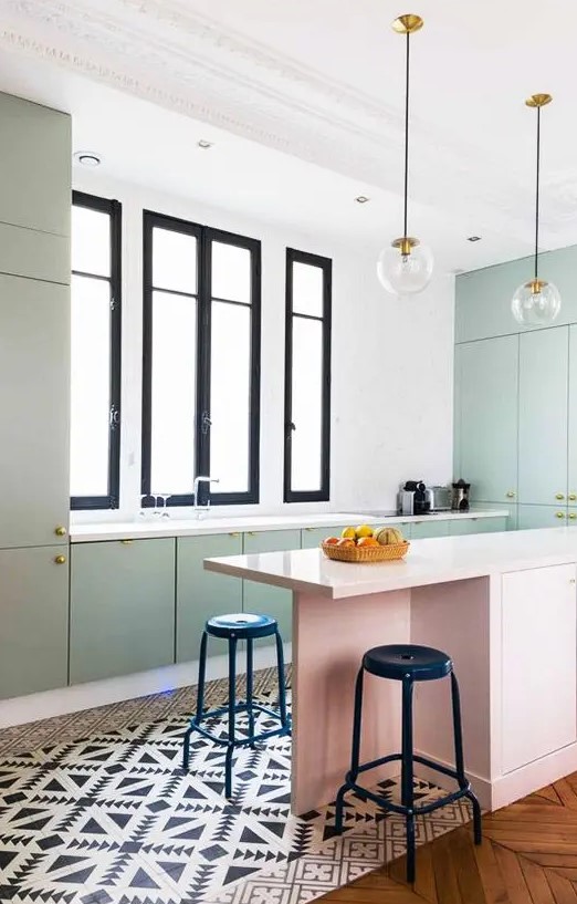 a beautiful pastel kitchen with pastel green cabinets and a pink kitchen island, black and white tiles and black stools