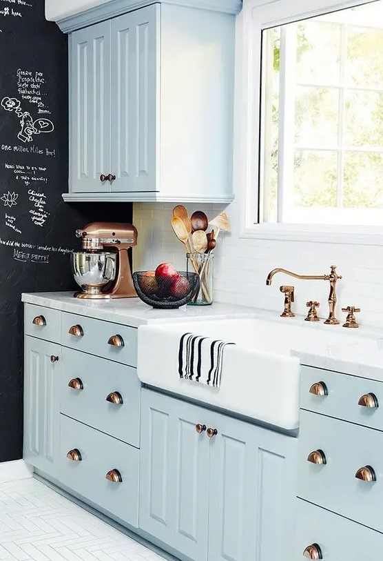 a pastel blue farmhouse kitchen with shaker cabinets, a white stone countertop and white tile backsplash, and a chalkboard wall