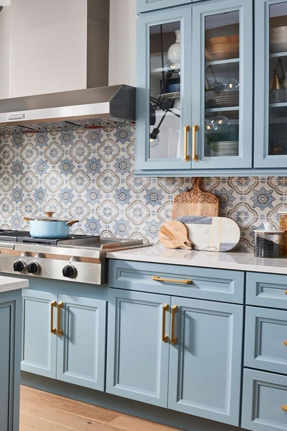 A pastel blue farmhouse kitchen with shaker cabinets, white granite countertops, and a bold printed tile backsplash is wow