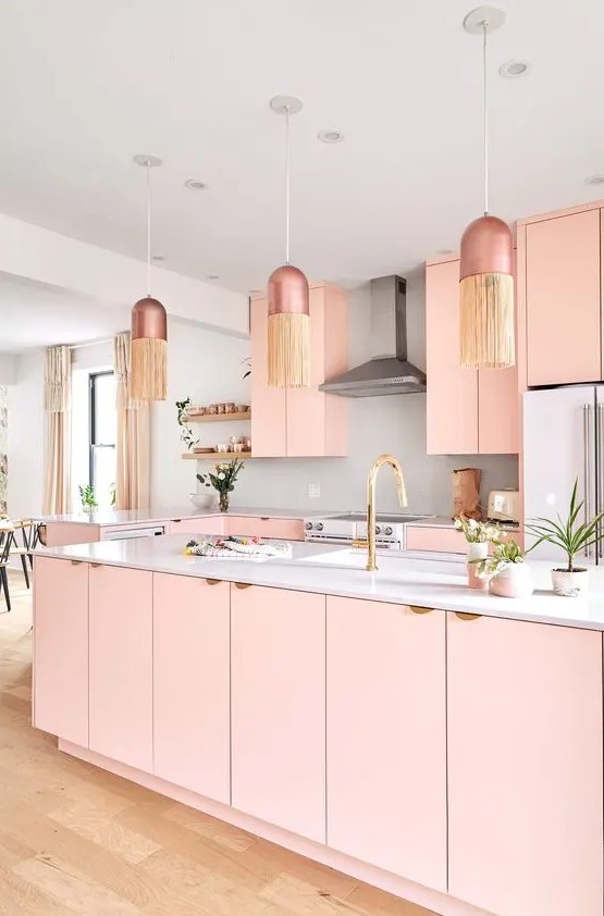 a pastel pink kitchen with simple cabinets, a large kitchen island, a white backsplash and countertop, hanging lamps with fringe