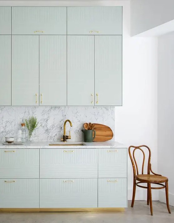 a sophisticated light green kitchen with geo-facades, a white marble backsplash and countertops, and gold fixtures