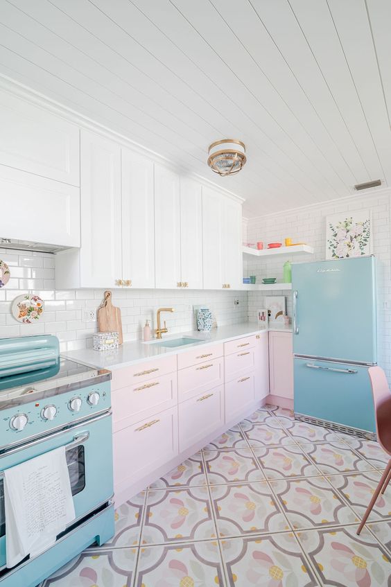 a two-tone kitchen with white and pale pink shaker cabinets, a blue refrigerator and stove, and a printed tile floor