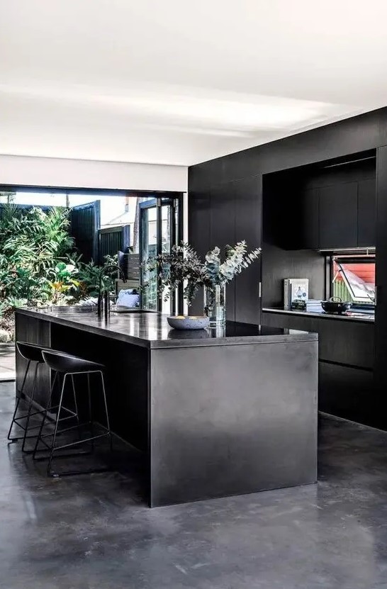 a modern, atmospheric kitchen with sleek black cabinets, a kitchen island, a glazed wall and an entrance to a courtyard