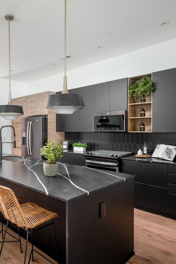 A modern matte black kitchen with a hexagonal tile backsplash, black marble countertops, black pendant lamps and woven chairs