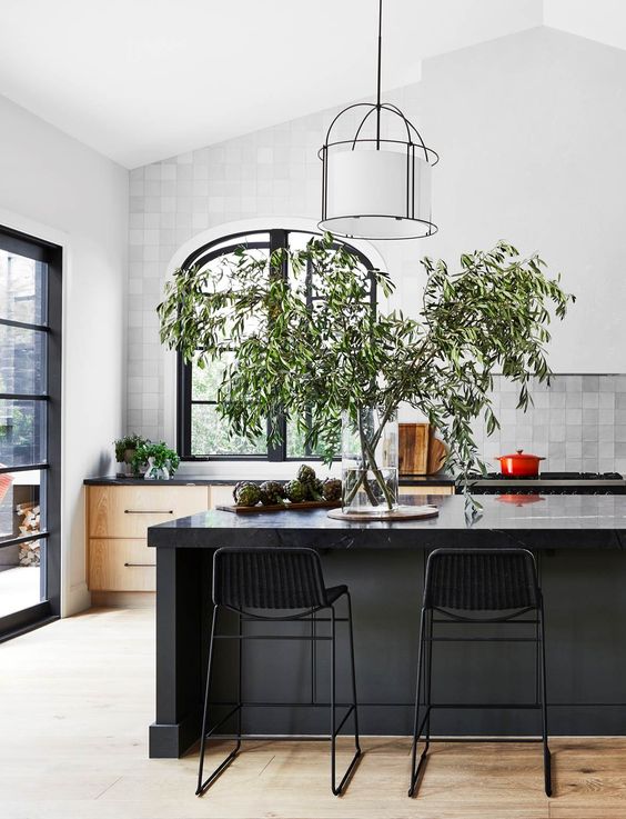 A beautiful kitchen with wooden cabinets, a gray tile backsplash, a black arched window and a black kitchen island with a marble backsplash