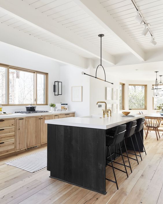 a farmhouse kitchen with wood cabinets, a black island, white countertops, a statement pendant lamp and a dining area