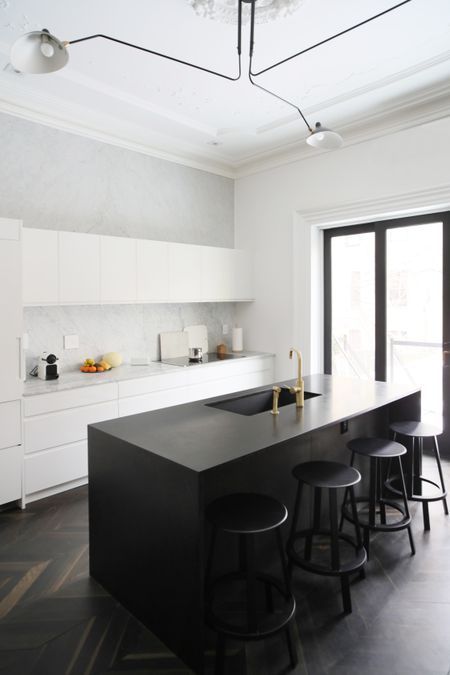 a minimalist black and white kitchen with elegant cabinets, a white stone backsplash, a black kitchen island and stools
