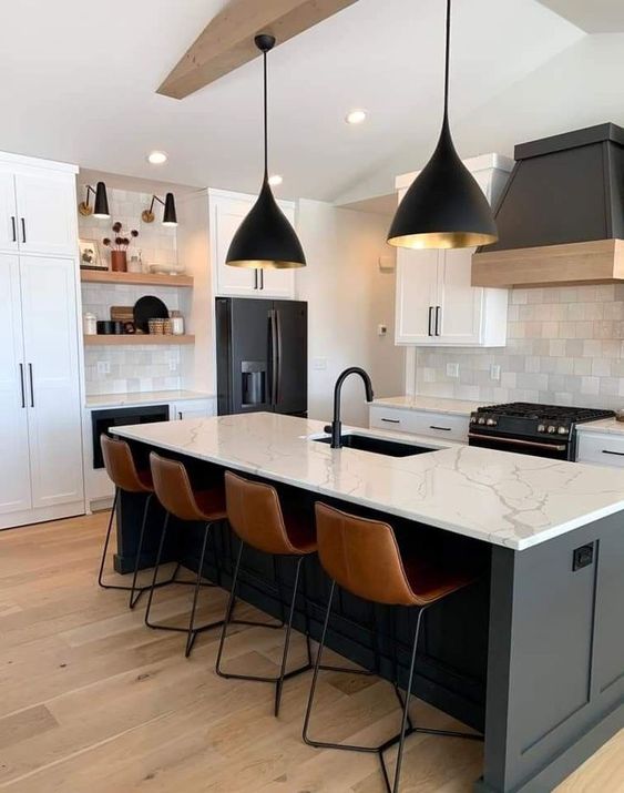 A modern black and white kitchen with white shaker cabinets, a black island, white countertops and backsplash, and black lamps