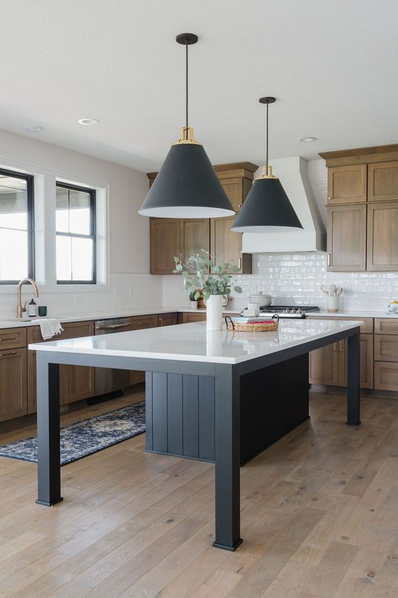 a modern, rustic kitchen with wooden cabinets, a white tile backsplash and a black kitchen island with a white countertop