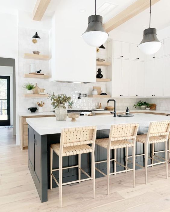 a neutral farmhouse kitchen with wood cabinets, white cabinets and open shelving, a black island, wicker stools and black lamps