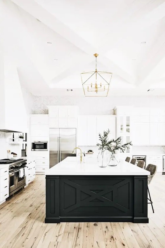 a white modern farmhouse kitchen with shaker cabinets, a black island, gold accents and lots of greenery
