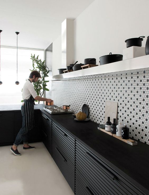 A bold black and white kitchen with a penny tile backsplash, black fluted cabinets and an open shelf for storing utensils