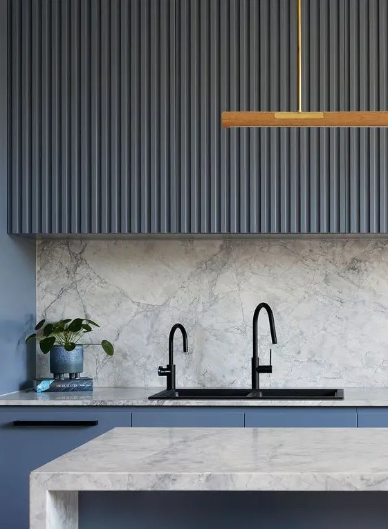 A modern kitchen with navy fluted wall units and sleek base units, a stone backsplash and worktops and black fittings