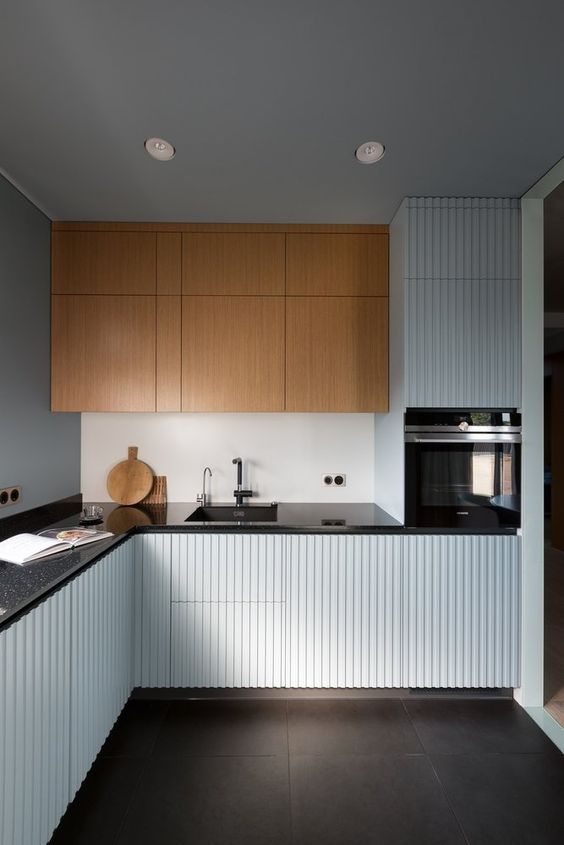 a minimalist kitchen with light blue, fluted and stained cabinets, black countertops and black fixtures