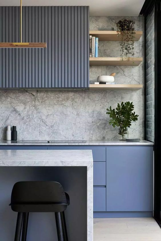 a minimalist but bold kitchen with fluted and elegant periwinkle cabinets, a gray marble backsplash and countertops