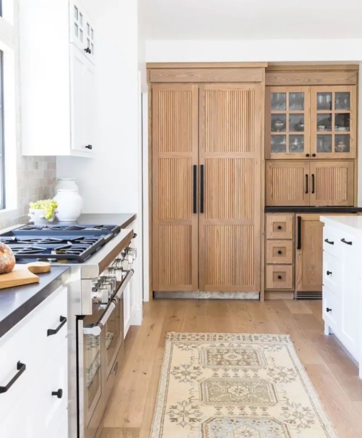 A modern farmhouse white shaker style kitchen with stained fluted cabinets and black fixtures