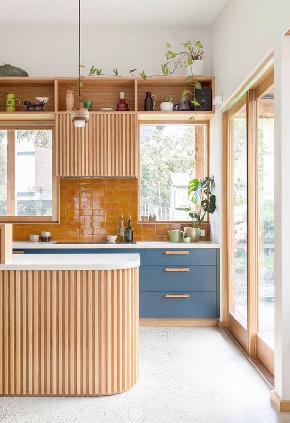 a modern kitchen with slate blue cabinets, a stained fluted cabinet as well as a stained fluted kitchen island and an orange tile backsplash