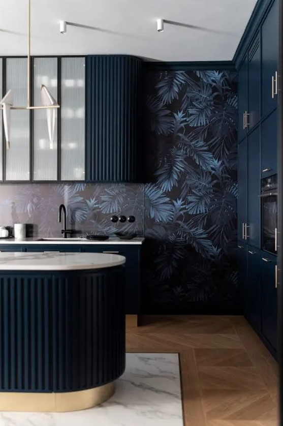 a moody and elegant kitchen with midnight blue curved and fluted cabinets and a matching kitchen island, dark wallpaper on the walls and black fittings