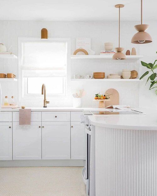a white Shaker-style kitchen with fluted cabinets, white stone countertops and brass hardware