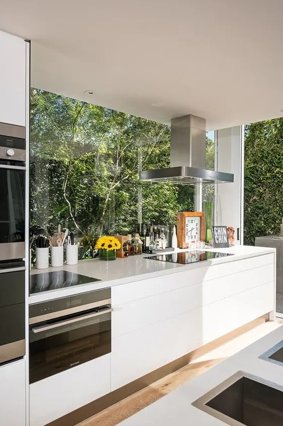 a modern white kitchen with elegant cabinets and stone worktops, as well as glazed walls opening onto the garden