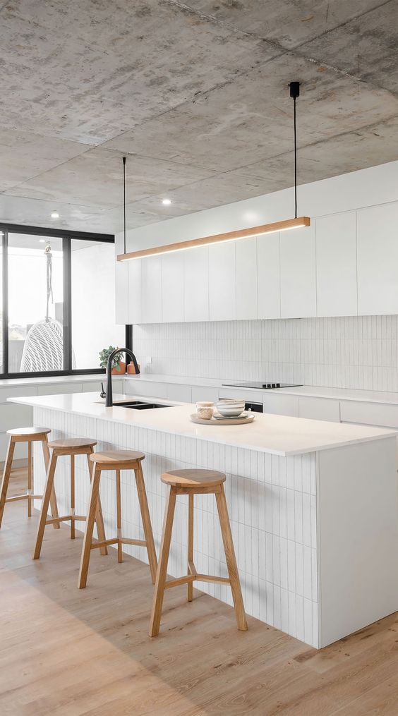 A modern white kitchen with sleek cabinets, a narrow tile backsplash and matching kitchen island decor with stained stools
