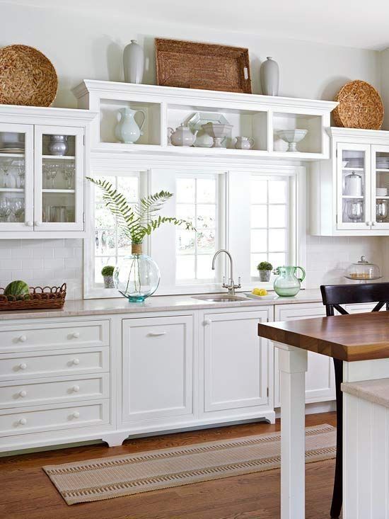 a cozy white kitchen with shaker-style cabinets, glass and regular cabinets, neutral stone countertops, baskets and vases