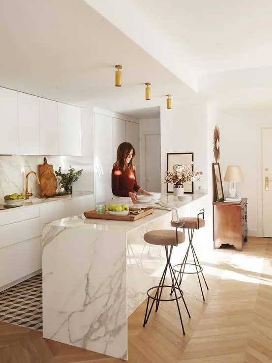 a modern white kitchen with sleek cabinets, a white marble kitchen island, matching countertops and a backsplash