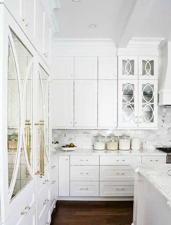 A beautiful white kitchen with brass details and mirrored and glass doors looks really luxurious