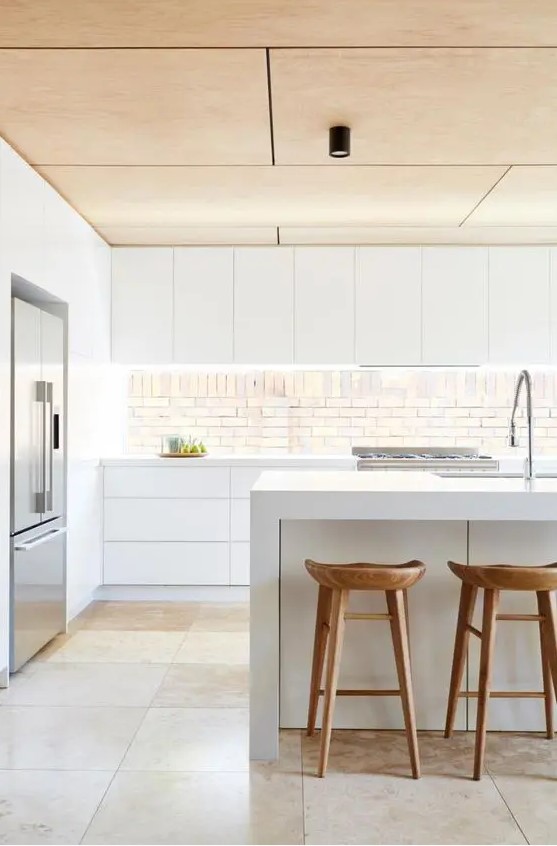 a minimalist white kitchen with a wooden ceiling, stools and an eye-catching splashback