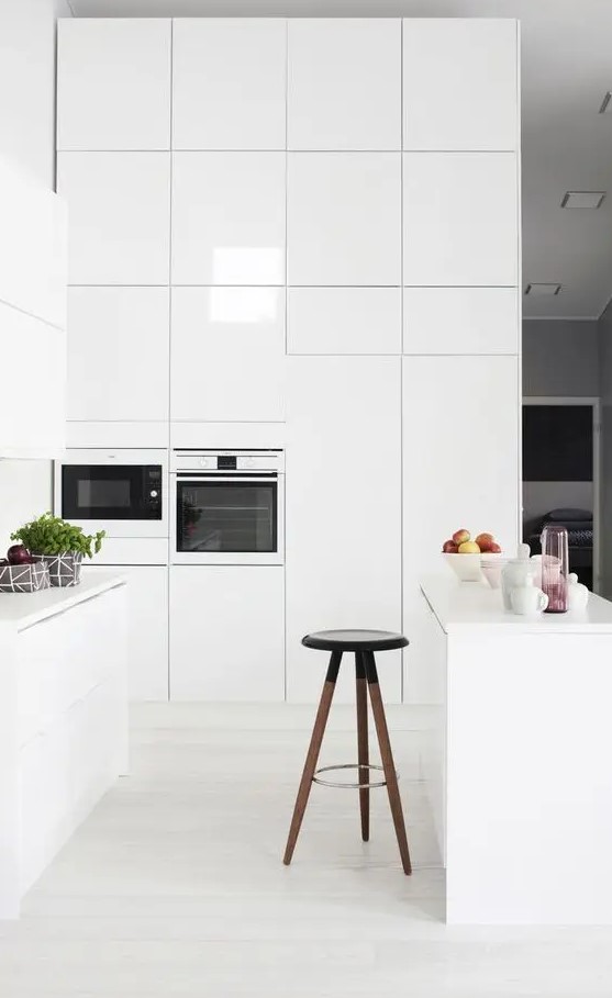 a minimalist white kitchen without handles, a stool and high cupboards in which everything can fit