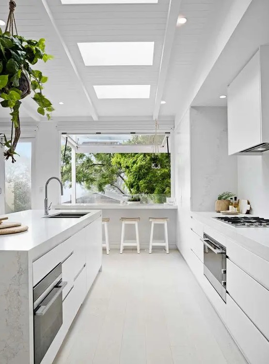 a minimalist white kitchen with marble countertops and a large window that opens into the outdoors as a dining area