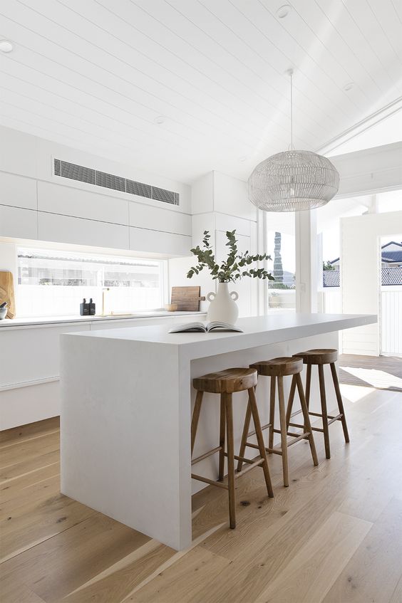 a minimalist white kitchen with sleek cabinets, a window backsplash, a large island and stained stools