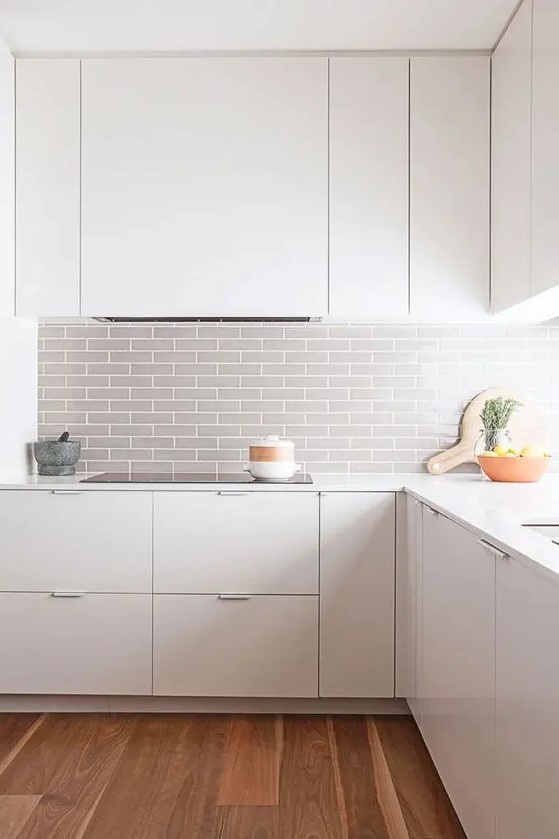 A modern white room is made even more striking with a gray tile backsplash and wooden floors