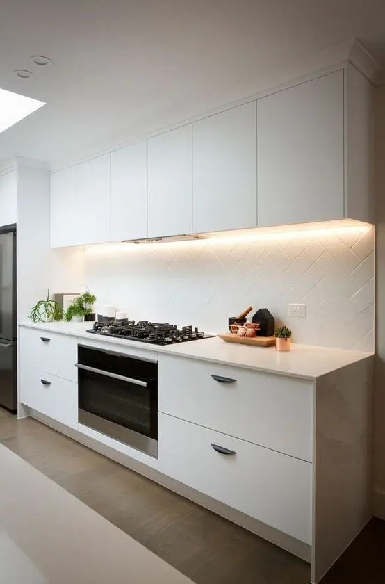 A modern white kitchen is made even more striking with lights and a geometric paneled backsplash