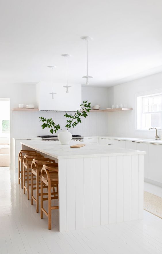 a calm white kitchen with modern cabinets, a wooden slat island, open shelving and stained stools