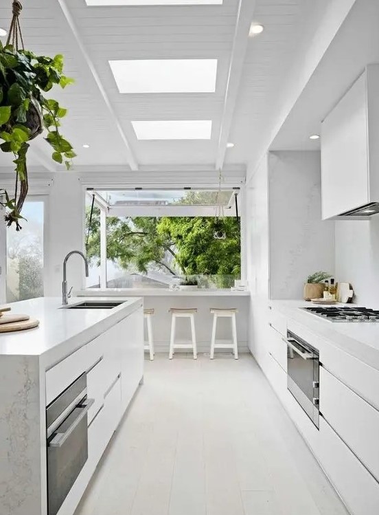 a serene white modern kitchen with sleek cabinets, a large island, white stone countertops and a backsplash