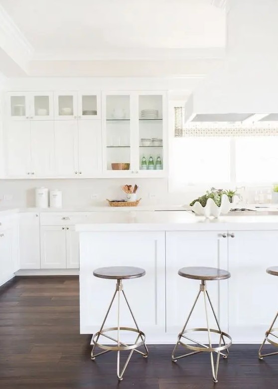 A simple white kitchen with glass cabinets and a large kitchen island gives an airy feel