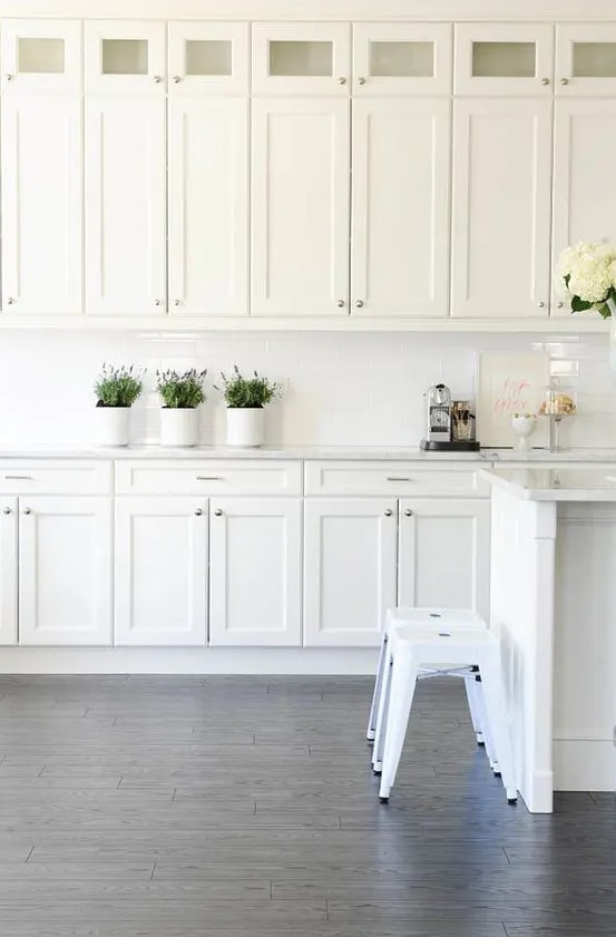 A white vintage kitchen with a white tile backsplash, stools and plenty of storage space