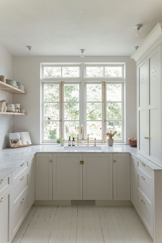 a small but cool white kitchen with shaker cabinets, white stone countertops, open shelving and gold fixtures