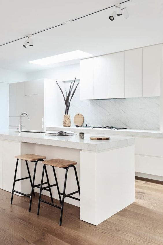 a white Japandi kitchen with elegant cabinets, a white marble backsplash and countertops, high stools and a skylight
