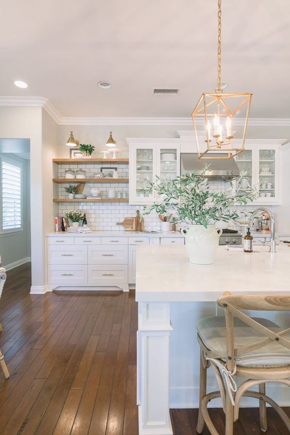 An inviting white farmhouse kitchen with shaker-style cabinets, a white subway tile backsplash, open shelving, and pendant lamps