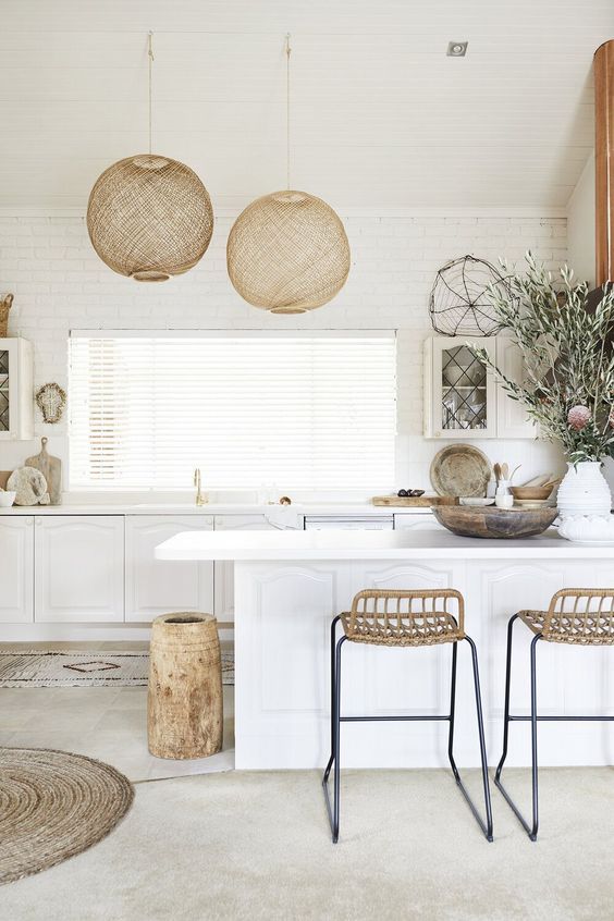 a white kitchen with vintage-inspired cabinets, tall wicker stools and a wooden vase, and wicker pendant lamps