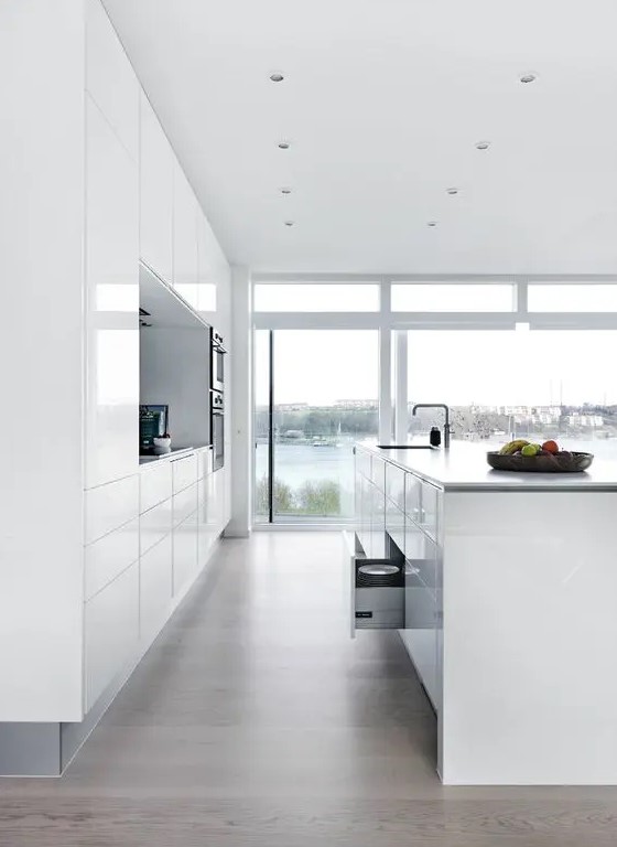 All-white, minimalist kitchen with sleek cabinets and great views, as well as a large kitchen island